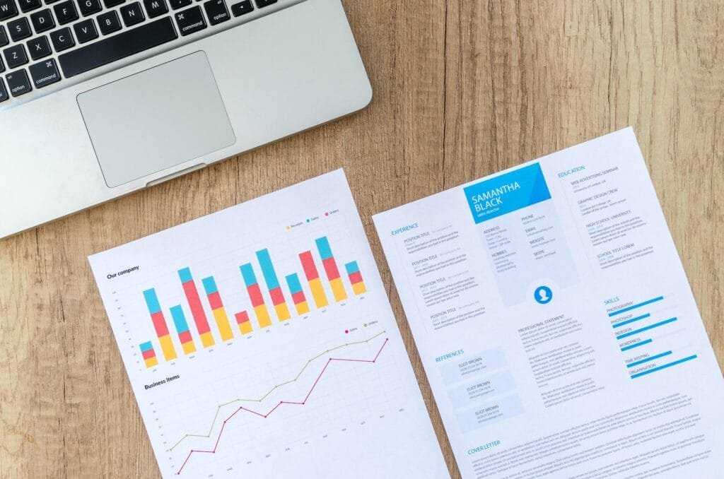 alt="An open laptop on a flat surface with paper showing graphs and data"