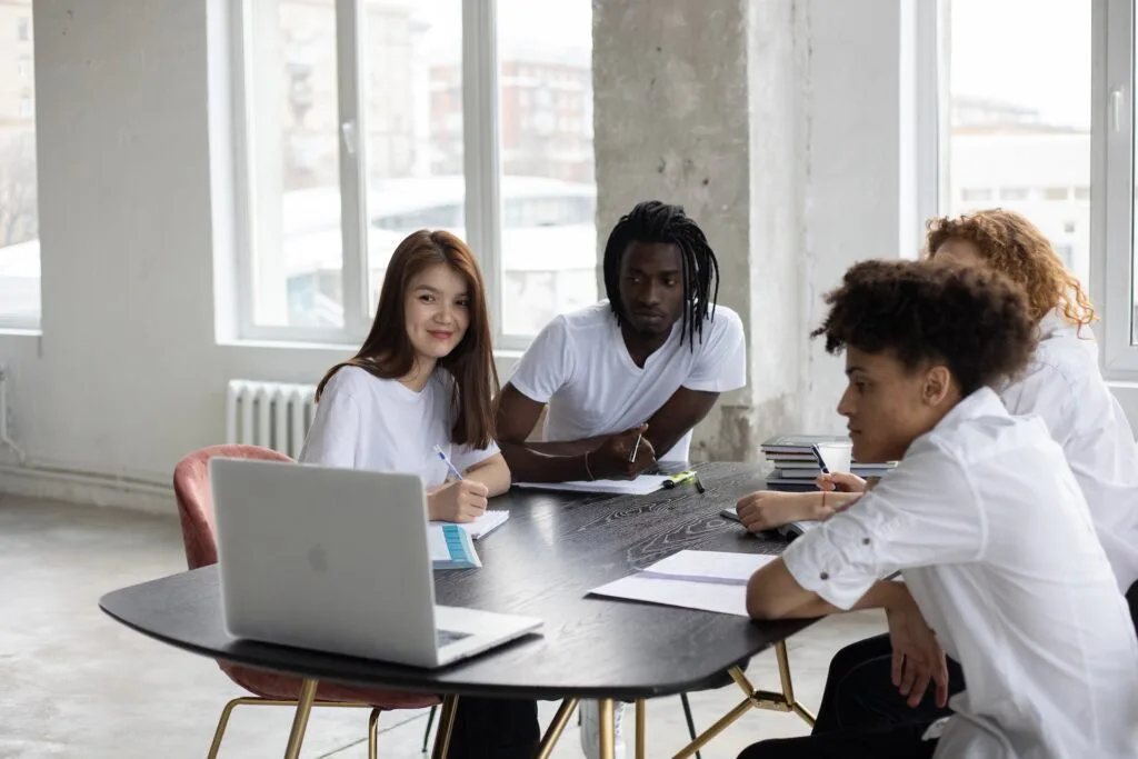 alt="A group of students gathered around a laptop with books and notebooks"