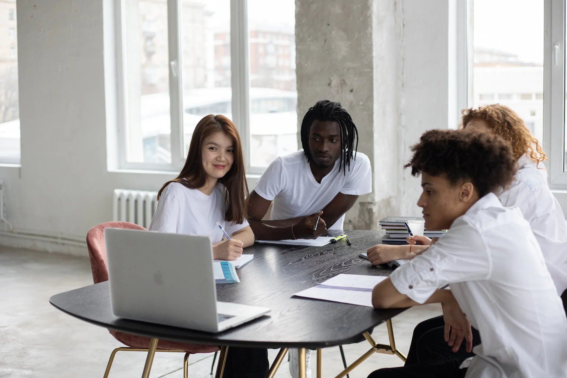 alt="A group of students gathered around a laptop with books and notebooks"