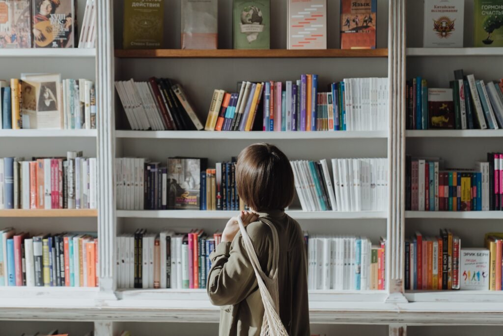 alt="a young woman standing in front of a book shelve filled with affordable education books"