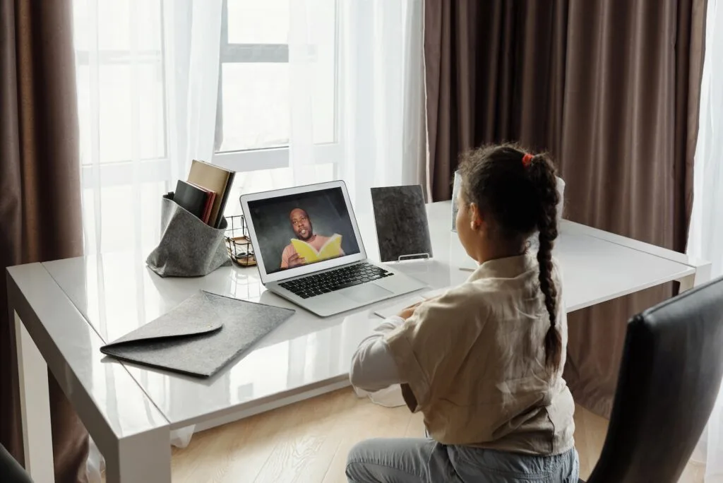 alt="a young student sitting in front of a computer with a teacher on the screen in an alternative education session from home"