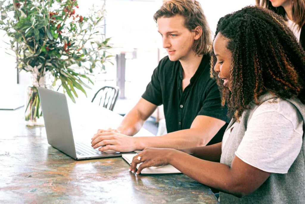 alt=" a man and two women in front of a laptop taking notes"