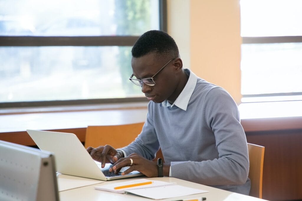 alt="a young student using a laptop on a table with pencil and paper around having an alternative education session"