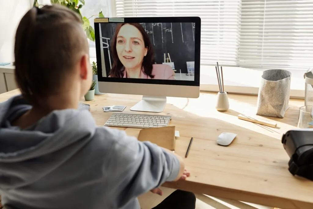 alt="a student facing a computer screen with the image of a teacher having an online alternative education session"