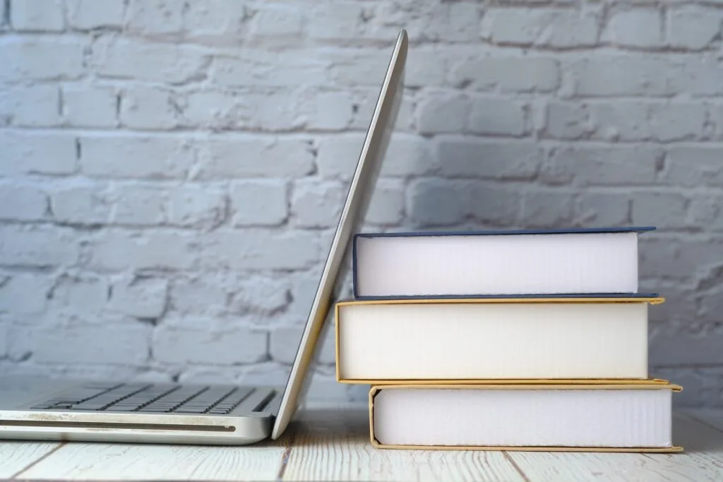 alt="an open laptop leaning against a stack of books representing education galaxy".
