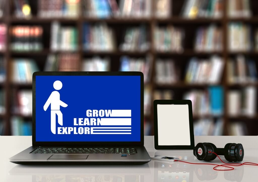 alt="An open computer with the words explore, learn, grow, next to a tablet and headphones as pert of education dynamics"