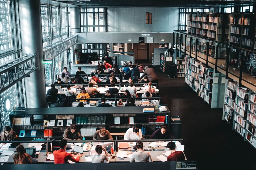 alt="Group of students with laptops studying in the library surrounded by books as part of education dynamics"