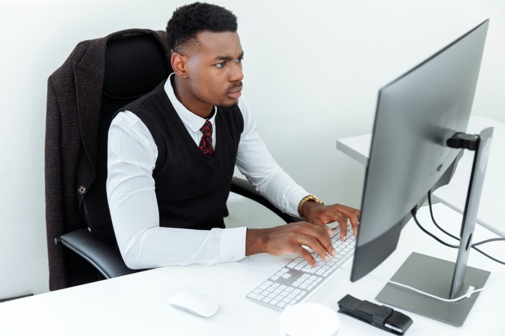 alt="A young man sitting in front of computer typing on a keyboard analyzing education background options"