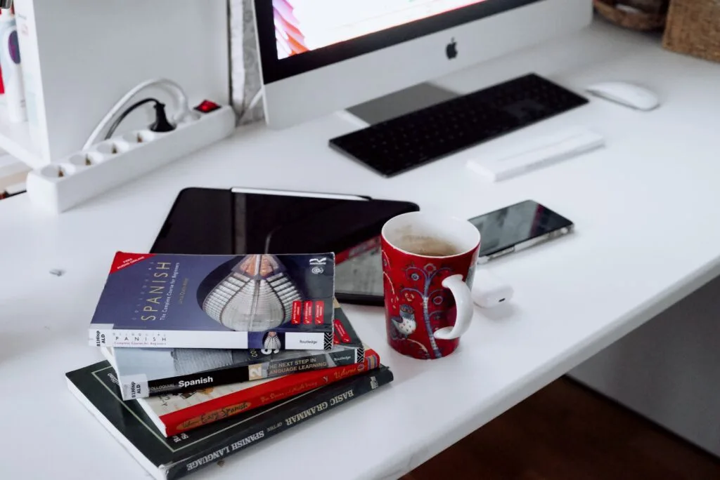 alt="A computer, a phone, a tablet pc and books with Spanish as titles, part of education in Spanish"