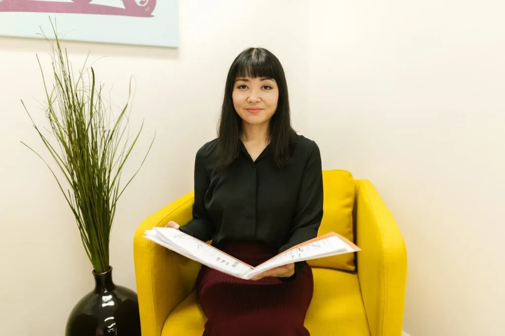 alt="A young woman sitting on a chair with an open folder comparing education background options"