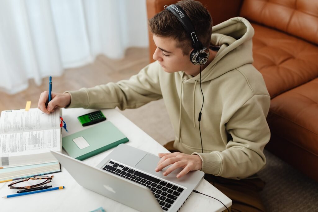 alt="A student focused on studying online with a book and headphone over his ears, part of education in Spanish"