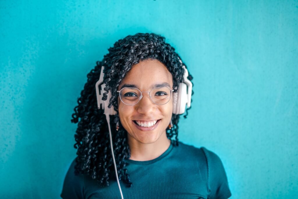 alt="A young female student listing to music on a headset smiling, part of education in Spanish"