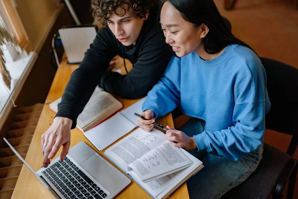 alt="A male and female student studying online on an laptop and some open books, part of education in Spanish"