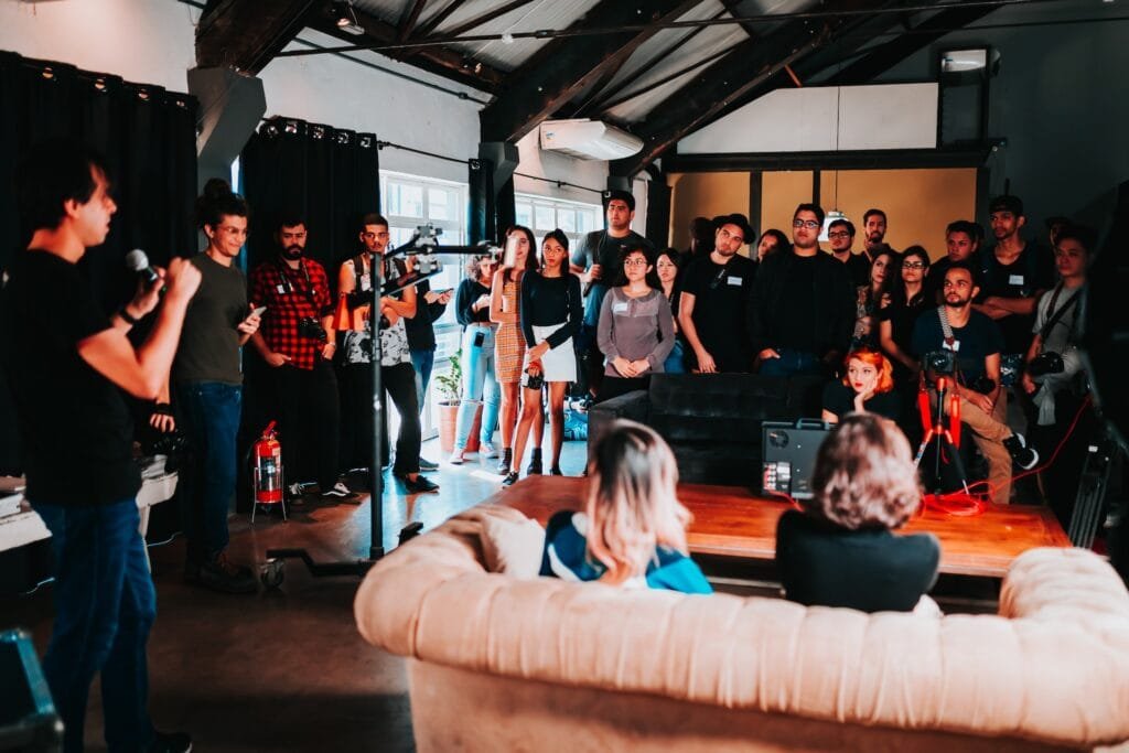 alt="A group of young adults in at a speaking event with a speaker on a microphone as part of education in Spanish"