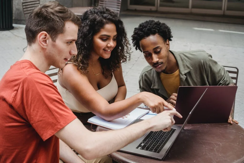 alt="Three students studying with laptops and open books as part of education in Spanish"